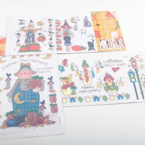 May include: Several sticker sheets with autumn and winter designs. The illustrations depict scarecrows, witches, snowmen, and harvest scenes. The sheets feature colourful illustrations and text such as "Gather the Harvest" and "Merry Christmas."