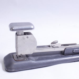 Könnte beinhalten: Ein vintage silberner und grauer Metallhefter mit einem Hebel an der Seite. Der Hefter hat eine Metallbasis und ein silbernes Oberteil.