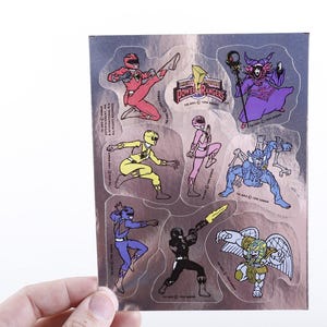 May include: A sheet of Power Rangers stickers featuring various characters in action poses. The stickers include the Power Rangers logo and character illustrations in vibrant colors like red, yellow, pink, blue, and black.