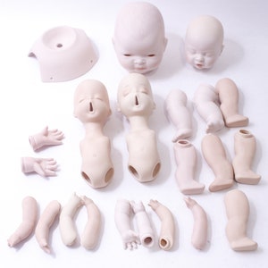 May include: A set of unpainted porcelain doll parts, including two heads, two torsos, two pairs of arms, four legs, and a head base. The doll parts are all white and have a smooth, matte finish.