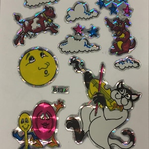 Könnte beinhalten: Ein Bogen mit bunten, holografischen Aufklebern, die eine Kuh zeigen, die über eine Wolke springt, eine Katze, die Geige spielt, einen lächelnden Mond, einen roten Hund, einen Löffel und einen rosa Kreis mit einem Gesicht sowie ein paar Sterne.