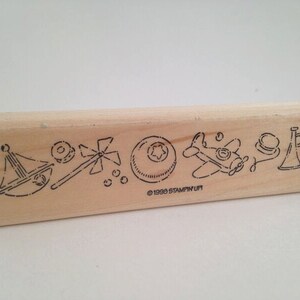 May include: Wooden stamp with a design of various toys including a sailboat, a pinwheel, a ball, an airplane, a hat, and a horn. The stamp is labeled "©1998 STAMPIN' UP!"
