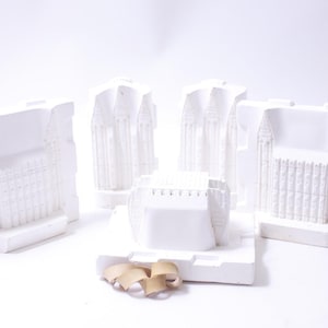 May include: Four white plaster molds of a building with intricate details. The molds are arranged in a square shape with a fifth mold in the center. The molds are on a white surface.