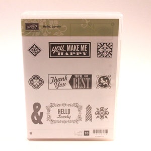 May include: A white package containing 10 clear rubber stamps with black ink. The stamps feature various designs including a heart, a flower, a diamond, and text that reads "You Make Me Happy", "Thank You", "You're the Best", "Hello Lovely", and "&".