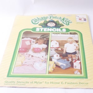 May include: A package of Cabbage Patch Kids stencils for home and fashion decor. The package features two children, one holding a pink balloon and the other holding a toy wagon. The text on the package reads "Cabbage Patch Kids Stencils" and "Quality Stencils of Mylar for Home & Fashion Decor".