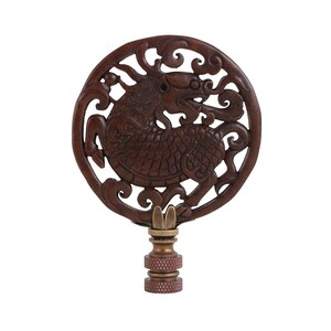 May include: A dark brown, carved wooden lamp finial featuring a detailed dragon design within a circular frame. The finial has a brass base and a decorative, ornate pattern. The dragon is depicted in a dynamic pose.