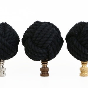 May include: Three black rope finials with different colored bases. The finials are made of thick black rope tied into a knot. The bases are silver, bronze, and gold.