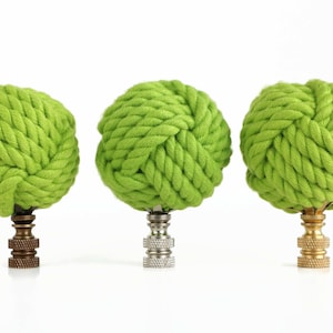 May include: Three lime green rope finials with a knot design. The finials are on a white background. The finials have different colored bases: brass, silver, and gold.