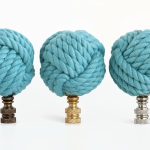 May include: Three teal blue rope finials with different colored metal bases. The finials are made of thick rope and are tied into a knot shape.