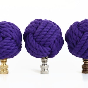 May include: Three purple rope finials with different colored bases. The finials are made of thick, twisted rope and have a round shape. The bases are gold, silver, and bronze.