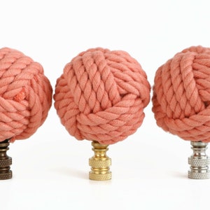 May include: Three coral-colored rope finials with different colored metal bases. The finials are made of thick, twisted rope and are perfect for adding a nautical touch to any room.