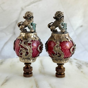 May include: Two red and silver finials with a dragon design and a lion finial on top. The finials are made of metal and have a shiny finish.