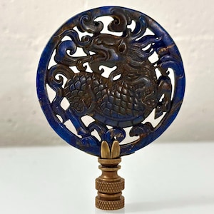 May include: A circular lapis lazuli lamp finial featuring an intricate openwork carving of a mythical creature. The deep blue stone is set into a brass base with a threaded connector, showcasing detailed scales and swirling cloud motifs.