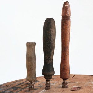 Könnte beinhalten: Drei Holzgriffe mit Metallsockeln. Die Griffe sind in verschiedenen Größen und Formen, einer ist rund, einer oval und einer rechteckig. Die Griffe sind alle aus dunklem Holz und haben ein abgenutztes, rustikales Aussehen.