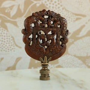 Può includere: Un terminale per lampada in legno marrone con intricate sculture di draghi e motivi floreali. Il terminale è montato su una base in ottone.