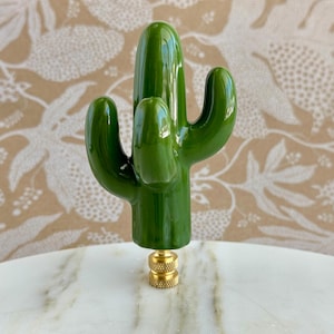 May include: A green ceramic cactus finial with a gold metal base. The cactus is a popular home decor item and can be used to add a touch of nature to any room.