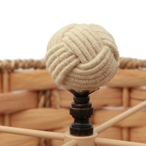 May include: A close-up of a woven lampshade with a rope finial. The finial is a decorative knot made of natural fiber rope.