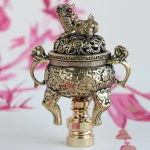 May include: Gold-toned metal incense burner with intricate floral and dragon designs. The burner has a round base with three legs and a removable lid.