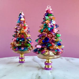 May include: Two colorful glass Christmas tree finials with a purple and gold base. The finials are decorated with a variety of colorful glass beads and glitter.