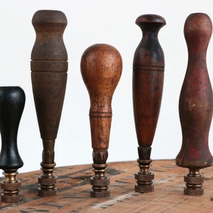 Puede incluir: Cinco remates de madera con bases de latón. Los remates son de diferentes formas y tamaños, y algunos tienen un color marrón rojizo.