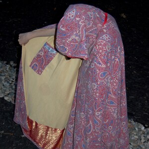 May include: A long, red and blue paisley patterned cape with a gold trim. The cape has a large pocket on the front.