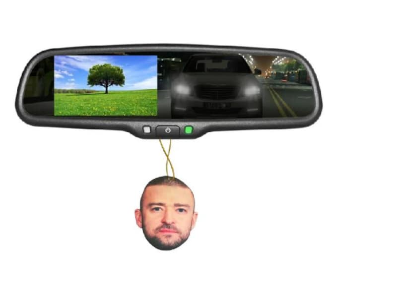 Peut inclure: Un r&eacute;troviseur de voiture avec un &eacute;cran int&eacute;gr&eacute; affichant un arbre dans un champ et une voiture. Un d&eacute;sodorisant Justin Timberlake est suspendu en dessous. Le miroir a un cadre noir et des boutons.