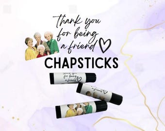 Peut inclure: Quatre tubes de baume à lèvres avec une étiquette blanche qui dit "Merci d'être un ami" avec un symbole de cœur. Les baumes à lèvres sont sur un fond violet et blanc.
