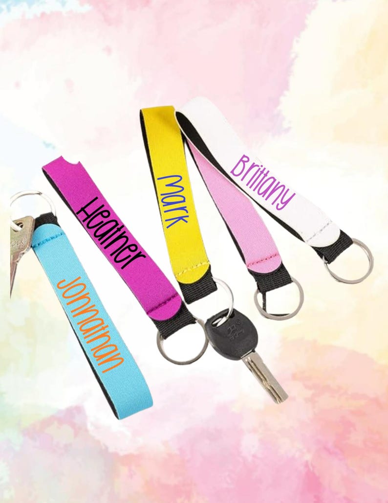 May include: Four fabric wristlet keychains with metal rings and attached keys. The wristlets are light blue with the name Jonathan, magenta with Heather, yellow with Mark, and white with Brittany printed in various colored fonts on the fabric.