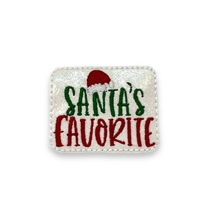 May include: White sparkly iron-on patch with red and green embroidery. The patch says "Santa's Favorite" with a red Santa hat above the text.