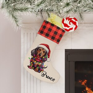 May include: A personalized Christmas stocking with a red and black buffalo plaid cuff. The stocking features a dachshund dog wearing a Santa hat and surrounded by Christmas lights. The name "Bruce" is written in cursive on the stocking.