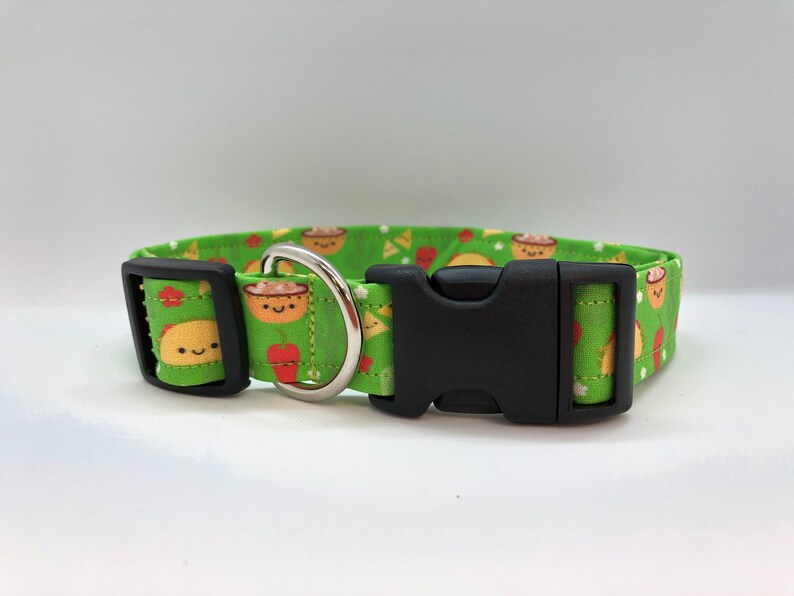 A green dog collar with a black buckle and a silver D-ring. The collar has a pattern of cartoon tacos, bowls of chili, and red peppers.