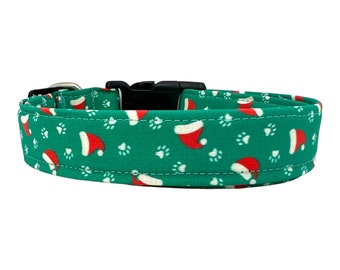 May include: A green dog collar with a white paw print and red Santa hat pattern. The collar has a black plastic buckle.