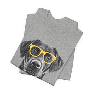 Pode incluir: Uma camiseta cinza com uma ilustra&ccedil;&atilde;o em preto e branco de um c&atilde;o usando &oacute;culos de sol amarelos.