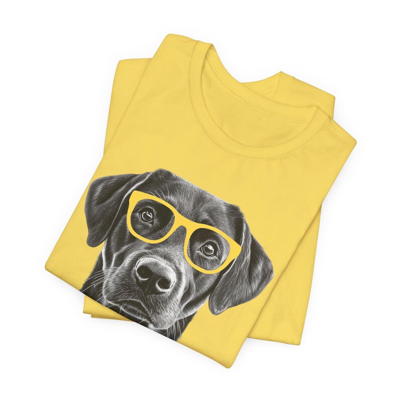 Pode incluir: Uma camiseta amarela com uma ilustra&ccedil;&atilde;o em preto e branco de um c&atilde;o usando &oacute;culos de sol amarelos.