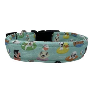 May include: A turquoise blue dog collar with a repeating pattern of dogs in various swimming poses, including floating on their backs, swimming with a ball, and riding a rubber ducky.
