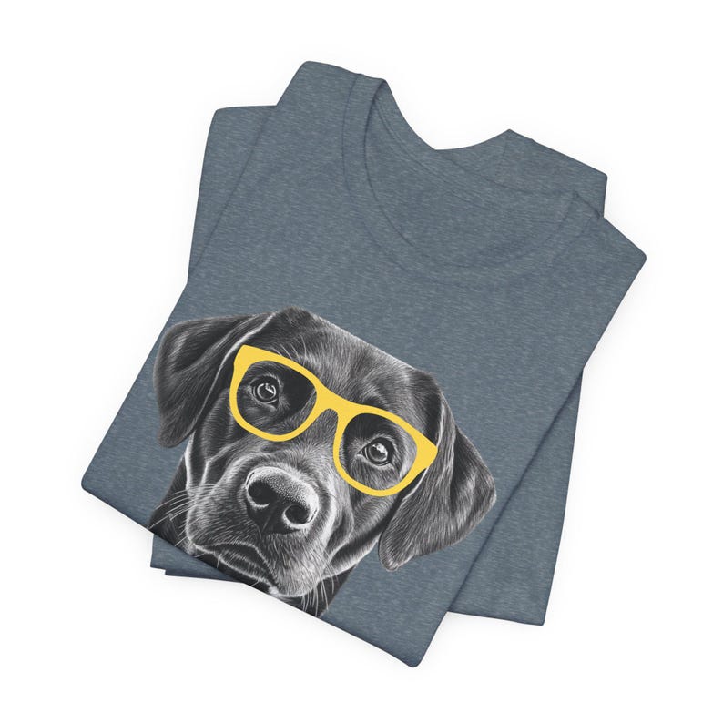 Pode incluir: Uma camiseta azul escura com uma ilustra&ccedil;&atilde;o em preto e branco de um Labrador Retriever usando &oacute;culos de sol amarelos.