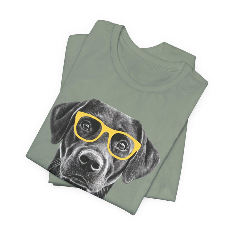 Pode incluir: Uma camiseta verde com uma ilustra&ccedil;&atilde;o em preto e branco de um c&atilde;o usando &oacute;culos de sol amarelos.
