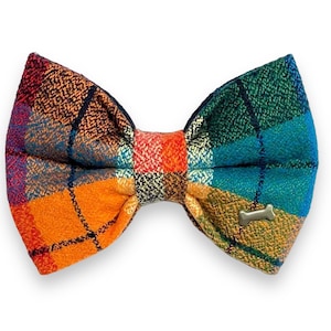 May include: A plaid bow tie for pets in shades of orange, blue, green, and yellow with a small gold bone charm.