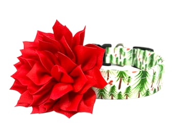 May include: A red fabric flower attached to a green and white dog collar with a pattern of pine trees and red berries.