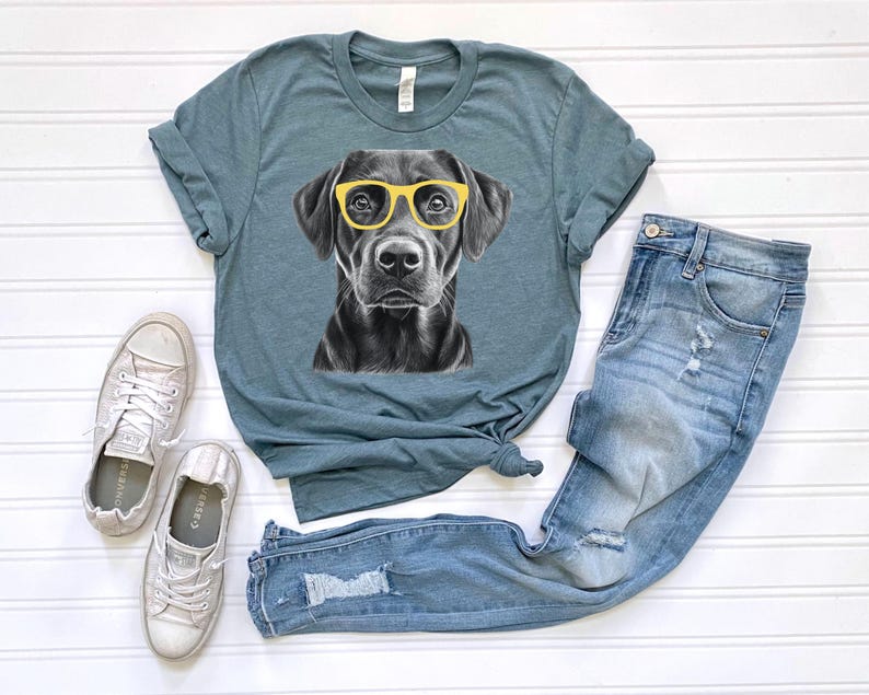 Pode incluir: Uma camiseta azul turquesa com uma ilustra&ccedil;&atilde;o em preto e branco de um c&atilde;o usando &oacute;culos de sol amarelos. O c&atilde;o est&aacute; olhando diretamente para a c&acirc;mera. A camiseta &eacute; combinada com jeans azul claro e t&ecirc;nis brancos.