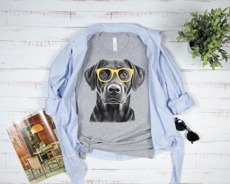 Pode incluir: Uma camiseta cinza com uma ilustra&ccedil;&atilde;o em preto e branco de um c&atilde;o usando &oacute;culos de sol amarelos.