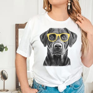 Pode incluir: Camiseta branca com uma ilustra&ccedil;&atilde;o em preto e branco de um Labrador Retriever usando &oacute;culos de sol amarelos.