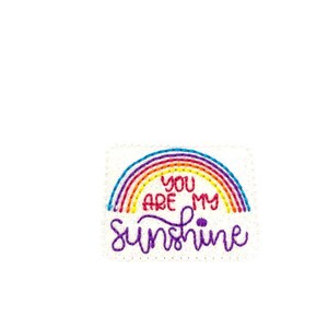 May include: Embroidered patch with a rainbow and the text "You are my sunshine" in purple.