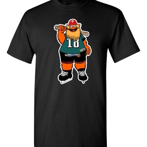May include: Black t-shirt with a cartoon mascot wearing a green jersey with the number 18, a red hat, and holding a baseball bat. The mascot has an orange body, a brown beard, and is wearing black ice skates.