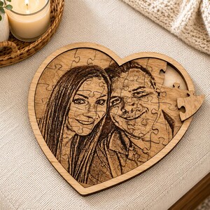 May include: A heart-shaped wooden jigsaw puzzle featuring a laser-engraved portrait of two people. The puzzle pieces are fitted together to form the image, with one piece slightly detached on the right side, revealing the light wood grain texture.