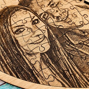 May include: A heart-shaped wooden jigsaw puzzle featuring a laser-engraved portrait of two individuals. The light-colored wood grain serves as the background for the dark, detailed etched image, which is divided into multiple interlocking puzzle pieces.