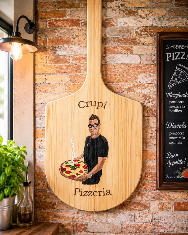 May include: A large wooden pizza peel featuring a hand-painted illustration of a person holding a steaming pizza. The text "Crupi" is printed above the figure, and "Pizzeria" is printed below. The wood grain is visible throughout the surface.