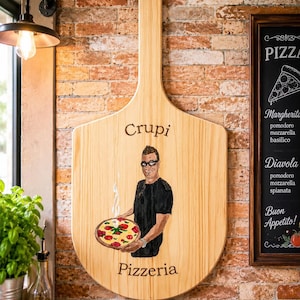 Może przedstawiać: Duża drewniana łopata do pizzy z ręcznie malowaną ilustracją osoby w czarnej koszuli trzymającej parującą pizzę. Napis "Crupi" znajduje się nad postacią, a "Pizzeria" poniżej, wykonany ciemnobrązową czcionką szeryfową.