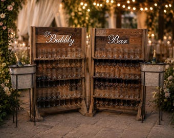 Puede incluir: Dos expositores de madera rústica con varios estantes llenos de copas de champán de cristal transparente. El expositor izquierdo tiene el texto The Bubbly y el derecho el texto Bar. Dos cubos de metal galvanizado contienen botellas de champán.