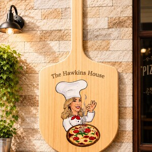 Może przedstawiać: Jasny drewniany szyld ścienny w kształcie łopaty do pizzy z napisem The Hawkins House. Grafika przedstawia kucharza w białej czapce i mundurze, wykonującego gest ok nad parującą pizzą z pepperoni, czerwoną sosem i roztopionym serem.